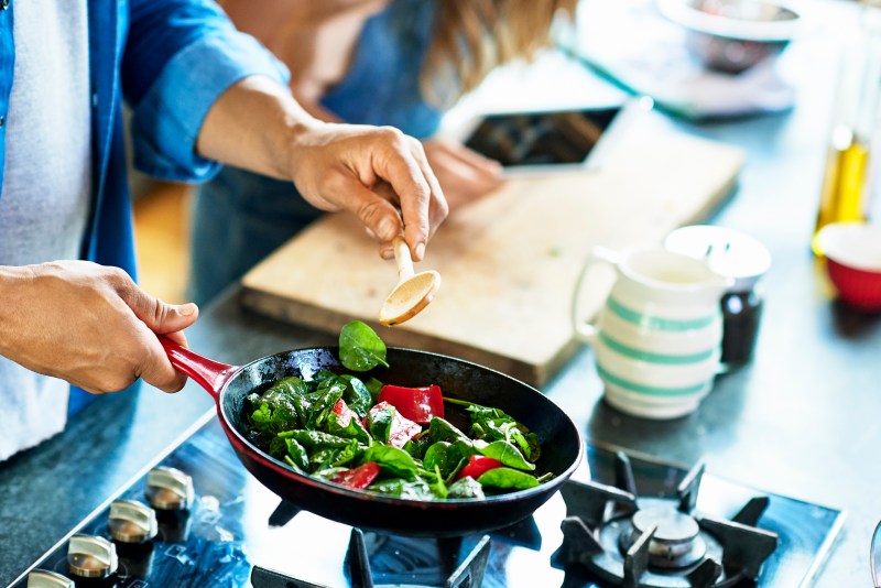 Close-up of a man holding frying pan with fresh vegetables and a wooden spoon