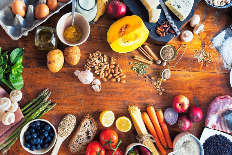 Colourful and healthy table composed with fruits and vegetables of many different types, meat, cheese, eggs, fish, spices and grains on a wooden table