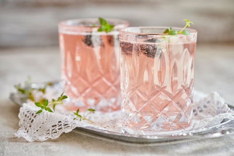 Two glasses of Rose cocktails with blueberry garnish on crocheted cloth on a metal tray