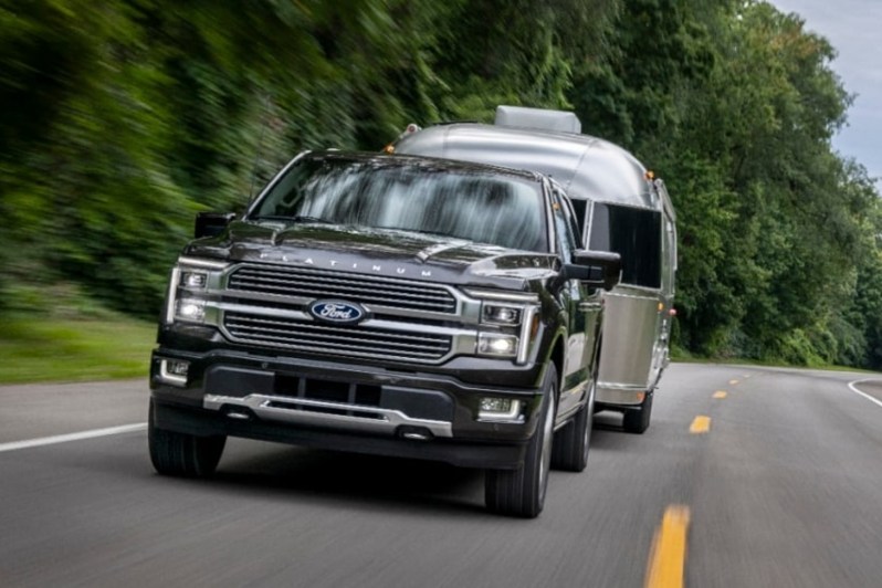 Ford Hybrid F-150 pulling an Airstream trailer on a two-lane road with trees next to the road.