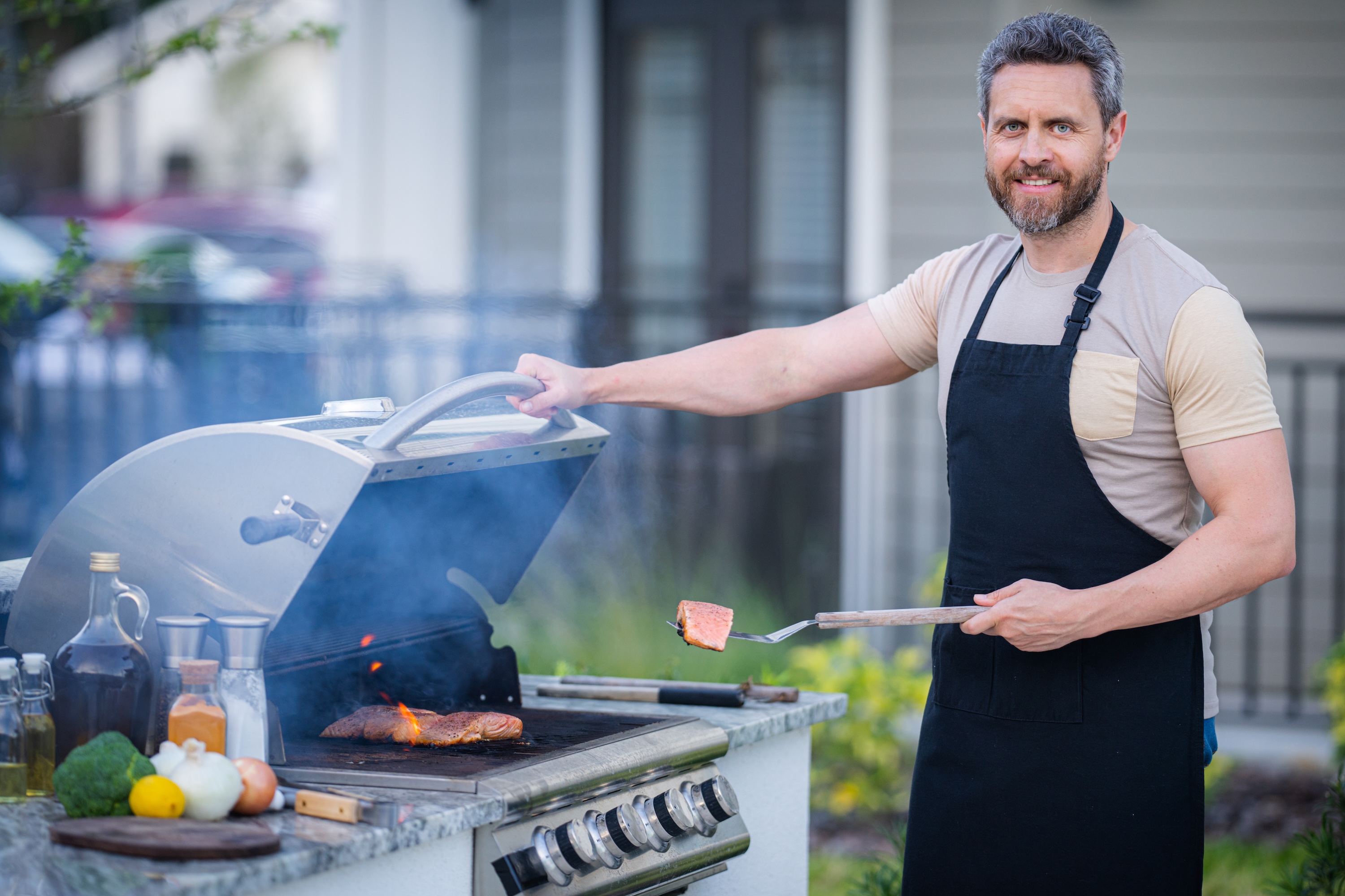 Male chef grilling and barbequing in garden. Barbecue outdoor garden party. Handsome man preparing barbecue meat. Concept of eating and cooking outdoor during summer time.