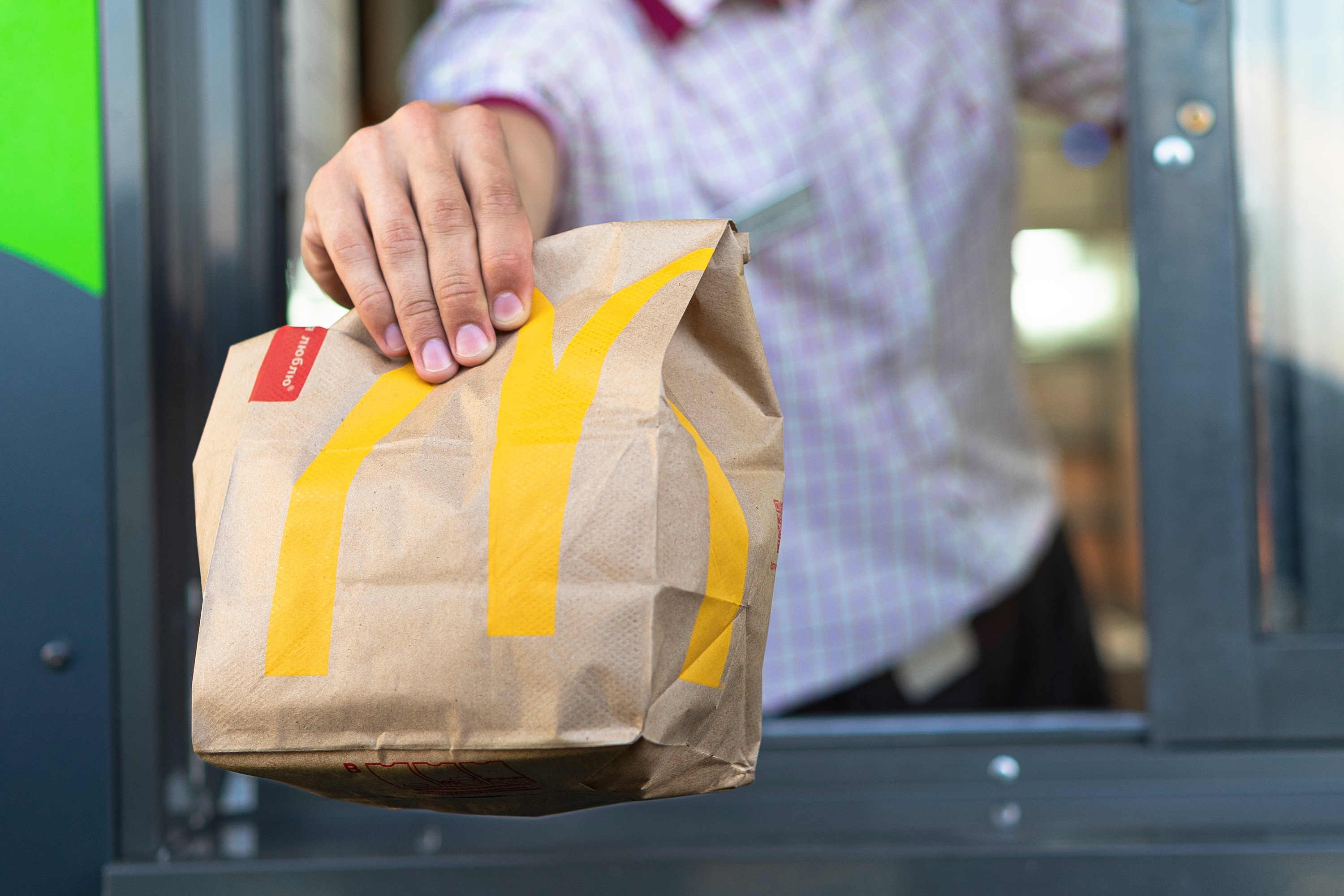 Sankt-Petersburg/Russia - July 21 2019: McDonald’s worker holding bag of fast food. Hand with a paper bag through the window of mcdonalds car drive thru service.