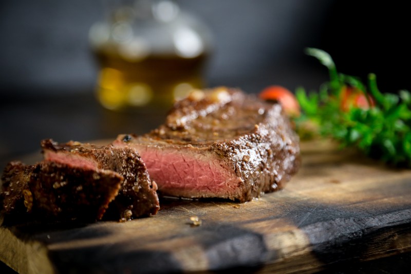 A plate of grilled meat and vegetables on a rustic wooden platter with a black background